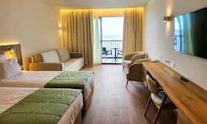 Ett hotellrum med två sängar, soffa, två fåtöljer, skrivbord och en balkong med utsikt. (AI-genererad text)