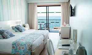 Ett hotellrum med en säng, ett skrivbord och utsikt över havet från en balkong. (AI-genererad text)