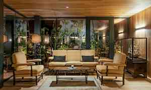 Interiör med sittgrupp bestående av soffa och fåtöljer framför en glasvägg med grönska utanför. (AI-genererad text)