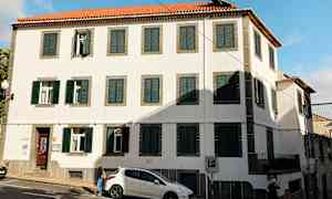 Byggnad med vita väggar, gröna fönsterluckor och röd taktegel. (AI-genererad text)