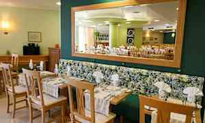 Restaurang med bord och stolar samt spegel på väggen. (AI-genererad text)