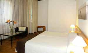 Ett hotellrum med två sängar, en fåtölj och ett bord med en blomvas. (AI-genererad text)