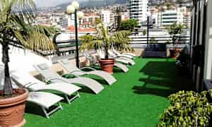 En terrass med konstgräs, solstolar och krukväxter. I bakgrunden syns stadens byggnader. (AI-genererad text)