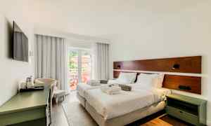 Ett hotellrum med två enkelsängar, vita sängkläder och kuddar. Rummet har en balkong med utsikt och är inrett med ett skrivbord och en TV. (AI-genererad text)