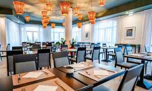 Restaurang med dukade bord och moderna stolar, med orangefärgade lampor i taket. (AI-genererad text)