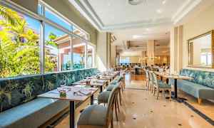 En ljus restaurang med moderna bord och stolar samt stora fönster med utsikt över grönska. (AI-genererad text)