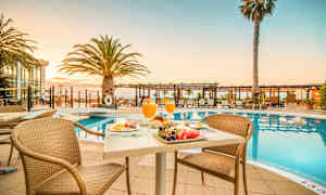 Ett frukostbord vid en pool med solstolar och palmer i bakgrunden. (AI-genererad text)