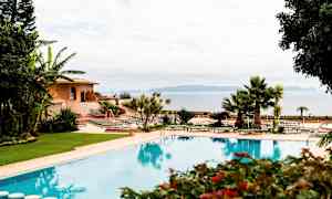 Bild av en utomhuspool omgiven av grönska, med solstolar och en byggnad i bakgrunden. (AI-genererad text)