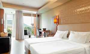 Hotellrum med två enkelsängar, sittgrupp och utsikt mot en bergig miljö genom glasdörr. (AI-genererad text)