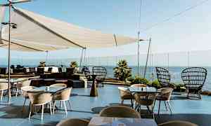 Utomhusterrass med bord och stolar, pergola och havsutsikt. (AI-genererad text)