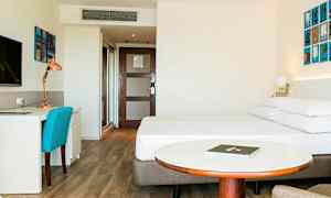 Hotellrum med en säng, skrivbord och stol, samt ett runt bord framför sängen. (AI-genererad text)