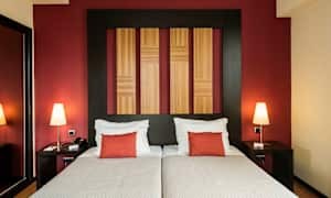 Två sängar med vita sängkläder och röda kuddar, en vägg med träpaneler och röd bakgrund. (AI-genererad text)