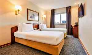 Bild av en hotellrum med två enkelsängar, ett fönster med gardiner, en väggmålning, och ett skrivbord med en stol. (AI-genererad text)