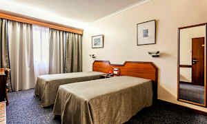 Bild av ett hotellrum med två enkelsängar, ett skrivbord och ett fönster med gardiner. (AI-genererad text)