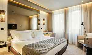 Ett modern inrett hotellrum med en dubbelsäng, väggmonterad TV och stora fönster med ljusa gardiner. (AI-genererad text)