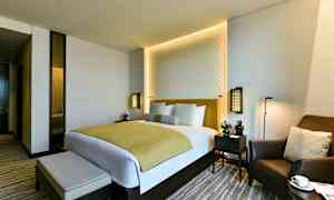 Ett modernt hotellrum med en dubbelsäng, två nattduksbord och en bekväm fåtölj. (AI-genererad text)