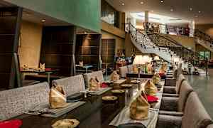 En elegant restaurang med bord dukade med servetter och tallrikar, samt en trappa i bakgrunden. (AI-genererad text)