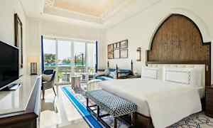 Hotellrum med en dubbelsäng, sittmöbler och en glasvägg som vetter mot en utomhusmiljö. (AI-genererad text)