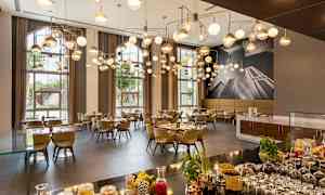 En elegant restaurang med moderna hängande lampor, dukade bord och stora fönster som släpper in naturligt ljus. (AI-genererad text)