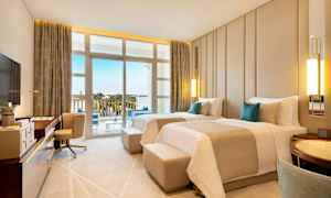 Ett hotellrum med två enkelsängar, skrivbord, fåtölj och balkong med utsikt över omgivningen. (AI-genererad text)