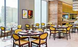 Bild av en ljus och modern restaurang med runda bord, gula stolar och ett välutrustat bufféområde. (AI-genererad text)