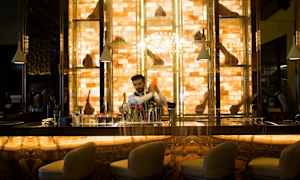 En vackert belyst bardisk med stolar i förgrunden och hyllor med uppställda prydnader i bakgrunden. (AI-genererad text)