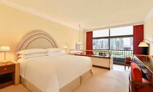 Hotellrum med dubbelsäng, nattduksbord och utsikt genom stora fönster över en stadsskyline. (AI-genererad text)