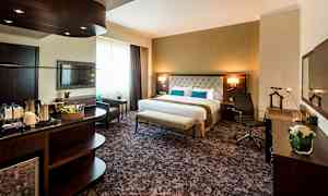 Ett hotellrum med en stor säng, två stolar och ett bord, samt en TV på väggen. Det finns en arbetsyta med kontorsstol och en välutrustad minibar. (AI-genererad text)