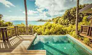 Utsikt från en träterrass och en pool över en tropisk trädgård och havet. (AI-genererad text)