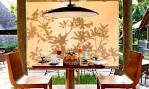 Ett dukat bord med frukostmat och dryck framför en beige bakgrund med skugga av lövverk. (AI-genererad text)