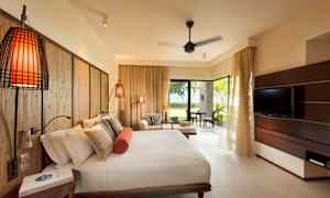 Ett hotellrum med en stor säng, soffgrupp och en tv, samt utsikt mot en grönskande trädgård. (AI-genererad text)