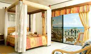 Ett sovrum med himmelsäng och utsikt över havet från en balkong. (AI-genererad text)