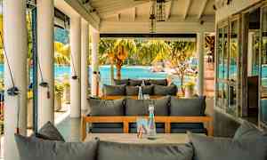 Uteservering med utsikt mot havet, möbler med gråa dynor. (AI-genererad text)