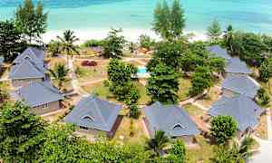 Flygfoto av bostadshus med trädgårdar och gångvägar vid en strand med turkost hav. (AI-genererad text)