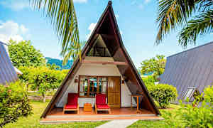 Ett A-format trähus med två solstolar framför, omringad av grönska. (AI-genererad text)