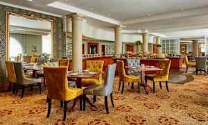 Ett elegant matsalsutrymme med flera dukade bord, bekväma stolar i senapsgul och grå färg samt dekorativa pelare och speglar. (AI-genererad text)