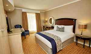 Ett hotellrum med en bäddad säng, en fåtölj, ett skrivbord och ett runt spegel på väggen. (AI-genererad text)