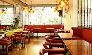 En restaurang med bord, stolar och bänkar vid fönster med dekorativa järnräcken. (AI-genererad text)