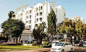 Vit byggnad med hotellskylt, omgiven av grönska och parkerade bilar. (AI-genererad text)