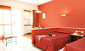 Ett hotellrum med två enkelsängar, röda sängkläder och en röd vägg, samt ett litet kök och en glasbord i bakgrunden. (AI-genererad text)