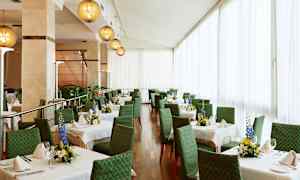 Ett ljus och elegant inrett matsalområde med gröna stolar och vita dukar på borden, dekorerade med färska blomsterarrangemang. (AI-genererad text)