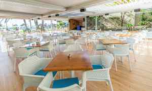 Utomhusrestaurang med bord och stolar framför panoramafönster. (AI-genererad text)