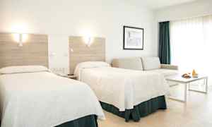 Ett hotellrum med två sängar, en soffa, ett bord och en frukostservering. (AI-genererad text)