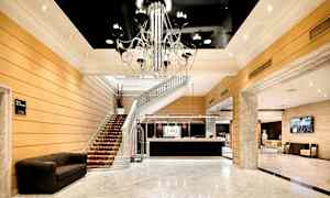 En hotellobby med marmorgolv och en elegant ljuskrona. En trappa leder upp från lobbyn och receptionen är synlig. (AI-genererad text)