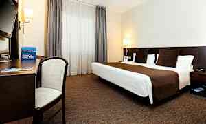 Ett hotellrum med en dubbelsäng, skrivbord, stol och stora fönster med gardiner. (AI-genererad text)