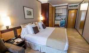 Ett hotellrum med en stor säng, kuddar, sängbord och en liten köksdel med skåp. (AI-genererad text)