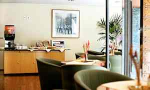 En kaffestation och sittgrupp i ett hotell eller kafé. En koppautomat och mellanmål finns på ett skåp. (AI-genererad text)