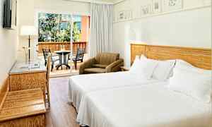 Ett hotellrum med två enkelsängar, en fåtölj och en möblerad balkong i bakgrunden. (AI-genererad text)