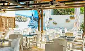 En utomhusrestaurang med vita stolar och bord. En vägg har en stor bild av en strandpromenad. (AI-genererad text)