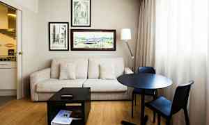 Ett rum med soffa, bord och två stolar, väggdekorationer och ett litet kök. (AI-genererad text)